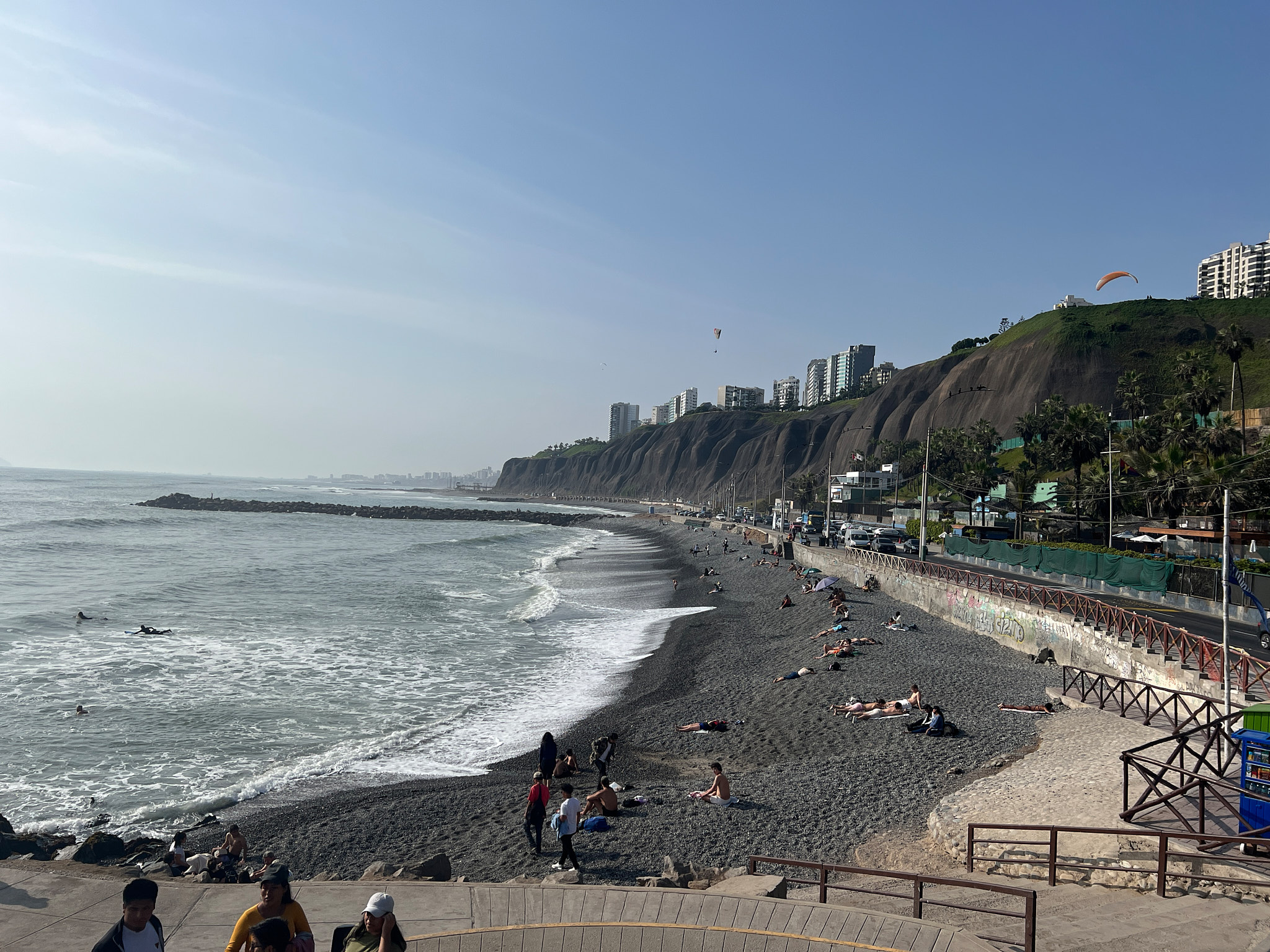 Pohled z pláže na útesy Miraflores s budovami, paraglideristy a Tichým oceánem