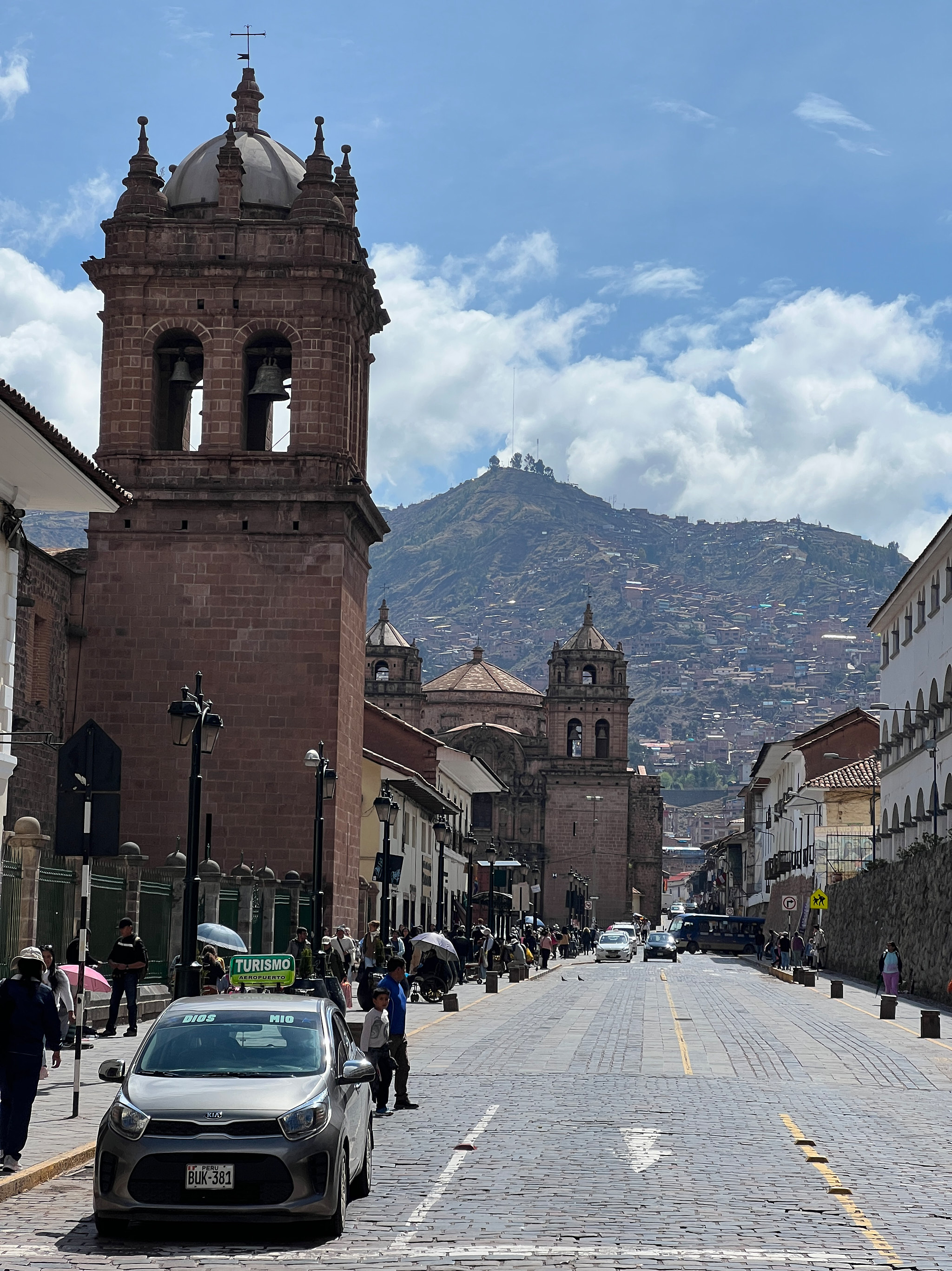 Cusco ulice s červenou věží kostela a kopci s domy v pozadí